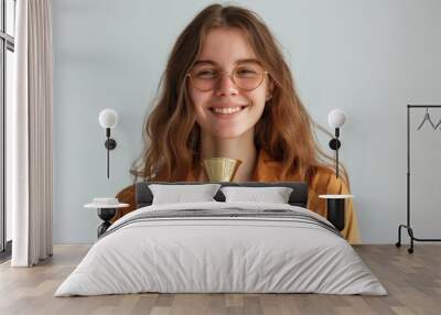 A smiling young caucasian woman in a casual attire holds a gold trophy, her eyes shining with pride. The image captures the essence of victory and the rewards of dedication. Wall mural