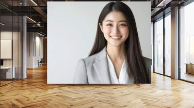 A young professional Asian woman in a gray suit, smiling as she gears up for a business meeting, highlights her potential and expertise. Wall mural