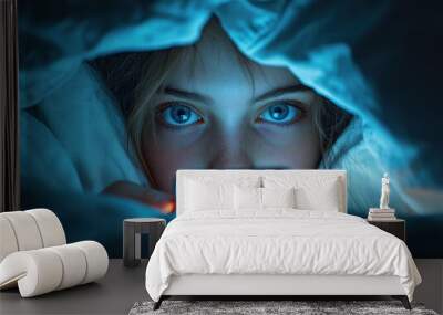 A young teenager concentrates on phone, illuminated by its blue screen while lying in bed at night. Wall mural