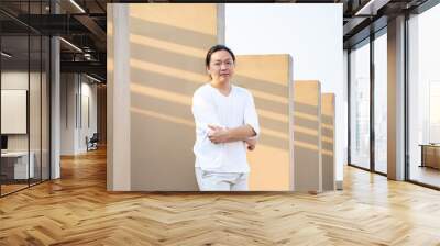 Asian long hair, Man in white long arm t-shirt is standing at the rooftop outdoor field with light brown wall bacgkround. Wall mural