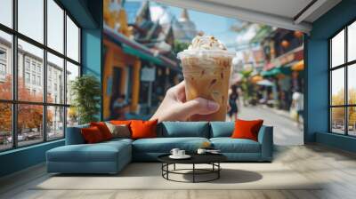 environment of streets and buildings, a plastic glass of coffee smoothie with a dollop of white whipped cream is held in hand, offering a refreshing treat amidst the urban hustle. Wall mural