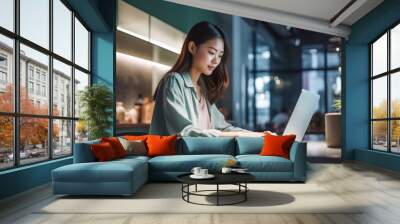 Happy Asian girl in formal office attire working joyfully on her laptop in a modern and cozy office setting. generative AI. Wall mural