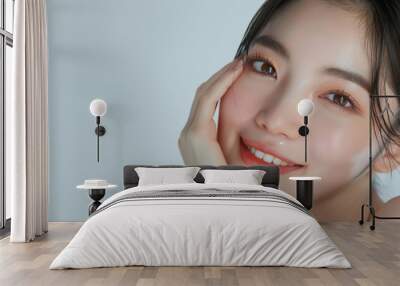 Portrait of beautiful young asian woman with clean fresh skin on white background, happy smile and hand touch face isolated over grey color backdrop. Beauty treatment concept. Wall mural