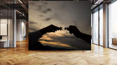 silhouette of hands holding jigsaw puzzles and joining together at sunset background, Teamwork and partnership concept Wall mural