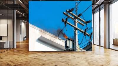 power pylon overload or electric short circuit at transformer on poles and fire or flame with smoke on blue sky Wall mural