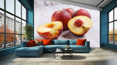 A few ripe juicy peaches on a light table. One peach is cut into two halves. Wall mural