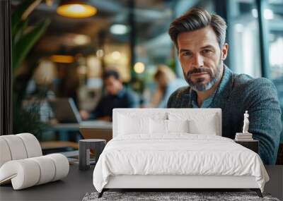 The creative process. Portrait of a man sitting at a table in an office using a digital tablet with colleagues working in the background, Generative AI Wall mural