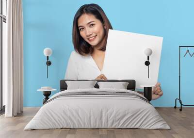 Portrait of young woman holding Empty white canvas frame for text or ad. isolated on blue background Wall mural