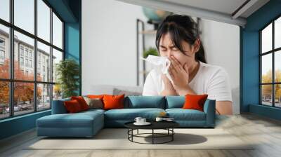 Young woman got a nose allergy sneezing sitting on the sofa at home.  Flu, Influenza, Sick, Fever, Illness. Healthcare and medical concept. Wall mural