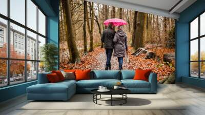 Senior couple walking in autumn forest with pink umbrella Wall mural