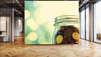 Close-up of a glass jar filled with gold coins, with a blurred green background. Wall mural