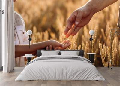 Farmer father playing with his little son in the field. A grain of wheat in the hands of a child. Dad - an agronomist pours a grain of wheat into his son's hands. Agriculture concept. Wall mural