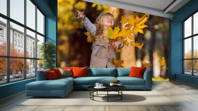 Little beautiful girl with long hair for autumn, holding leaves. Little girl in a beige coat in autumn park. The girl in the hands of a bouquet of yellow leaves. Autumn portrait Wall mural