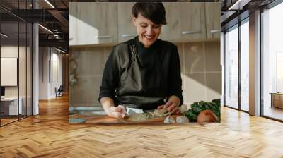 Portrait of happy smiling female chef preparing a recipe in the kitchen with vegetables. Woman cook chopping kale for vegetarian dish. Wall mural