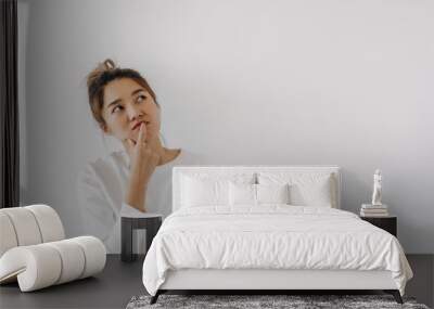 Asian Thai woman wear sweater bun hair, touching chin and mouth with doubt and curious face, have question thinking and looking at empty space, isolated on white background wall at winter. Wall mural