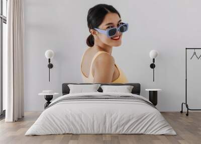 Asian Thai woman wear yellow top and blue sunglasses, chic and fashion, turn her back looking at camera and standing isolated over white background wall. Wall mural