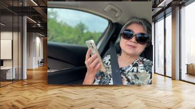 Happy elder mother, asian woman sitting in front seat, using mobile phone while traveling as passenger by car on holidays, happy life and insurance concept. Wall mural