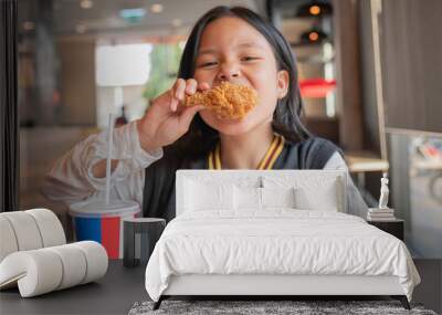 Close up portrait of a satisfied pretty  little asian girl eating fried chicken and french fries In the restaurant. Unhealthy food concept, close up Wall mural