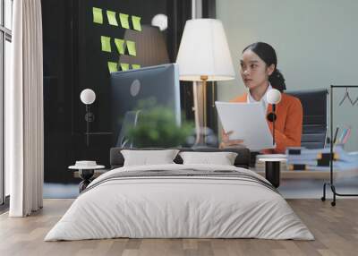 Young adorable Asian businesswoman working with work document during the night, working overtime at night. Wall mural