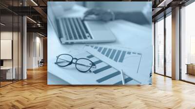 Business documents on office table with laptop computer and graph financial diagram and man working in the background Wall mural