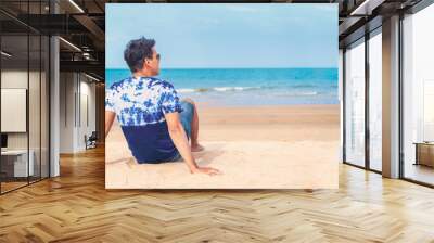 Happy young man in casual clothing wearing sunglasses and smiling at the beach. Handsome guy laughing at the beach and looking away. Cheerful guy enjoying summer vacation 
 Wall mural