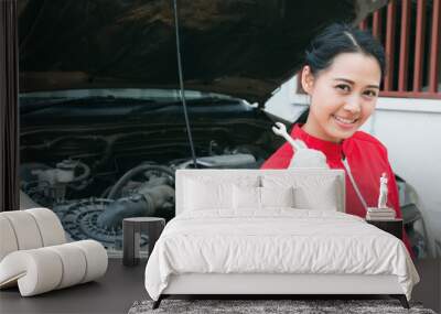 Portrait of smiling young female mechanic in red overalls holding a wrench in hand with car engine background, Concept of service or repair motor car, Detail of engine. Wall mural