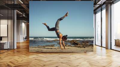 a beautiful brunette girl in gray leggings is engaged in fitness on the sand against the background of the sea Wall mural