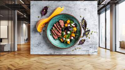 Baked pumpkin salad, spinach, tomato and beef in a white plate on a stone background, top view Wall mural