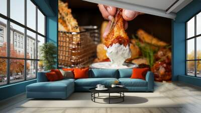 Hand holding grilled chicken legs dipping in sauce and set of grilled black pepper chicken background. Wall mural