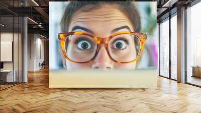 A photo of a person wearing stylish glasses, with their eyes peeking over the frame, set in a creative workspace. Wall mural