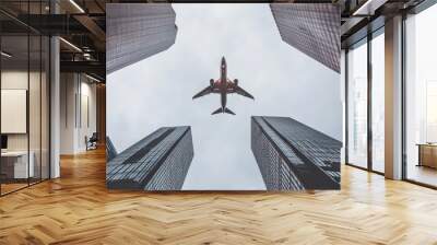 Airplane soaring above high-rise skyscrapers in a bustling financial district, capturing the essence of modern urban life and the dynamic nature of business and travel in the city Wall mural