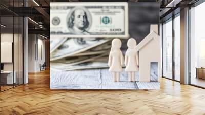 Two symbolic plastic figures stand in front of a conventional house, representing the dream of homeownership amidst a backdrop of numerous 100 USD bills, symbolizing wealth and prosperity Wall mural