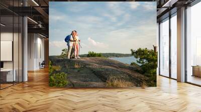 Active senior couple hiking on the top of rock, exploring. Mature man and woman Happily smiling. Nordic walking, trekking. Scenic view of gulf and sea. Healthy lifestyle. Finland. Wall mural