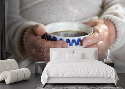 Close-up hands of old woman with mug of hot coffee. Senior lady sitting in chair with blanket. Warm and cozy, time to relax.  Wall mural