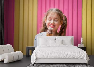 Cute little girl eating chocolate ice cream. Smiling and laughing. Colorful pink and yellow wall on background. Bright summer concept Wall mural