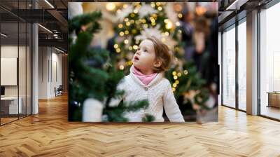 Cute little girl with open mouth in big shopping mall staring at the beautifully decorated christmas tree with lights.  Wall mural