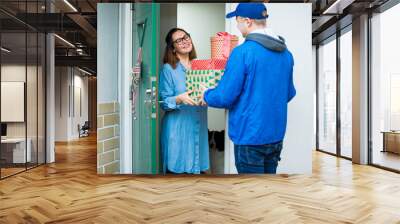 Delivery man bringing holiday packages. Woman at home standing in doorway, receiving parcels for Christmas gifts.  Wall mural