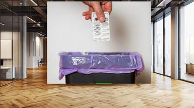 Hand putting expired medicine packages into bin with recycling sign for safe disposal. Person separating dangerous waste. Medical waste management Wall mural