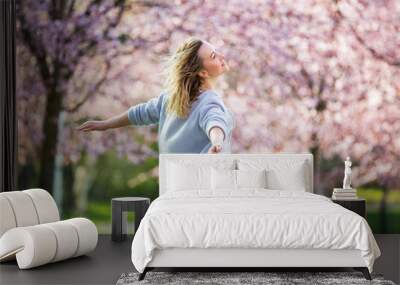 Young woman enjoying the nature in spring. Dancing, running and whirling in beautiful park with cherry trees in bloom. Happiness concept Wall mural