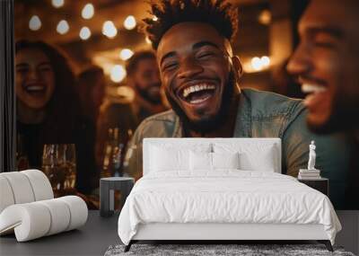 A cheerful young man in casual attire is captured laughing with friends at an evening gathering, as warm lights provide a cozy and inviting atmosphere. Wall mural