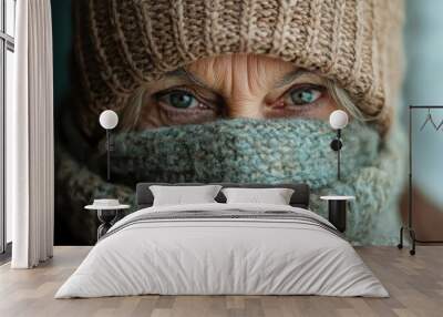 A close-up image of an elderly person donned in a brown hat and scarf, their brilliant eyes gazing intently, juxtaposed with the knitwear's texture. Wall mural