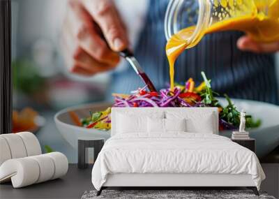 A fresh and vibrant mixed salad with various vegetables is being dressed with orange vinaigrette sauce by a person in a striped apron. The dish is perfectly colorful and appetizing. Wall mural