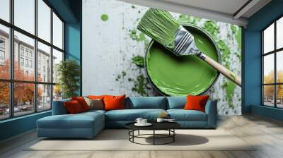 A paintbrush coated with green paint rests on the edge of an open paint can filled with the same green paint, all set against a white background with green paint splatters. Wall mural