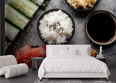 A variety of sushi ingredients such as rice, raw tuna and salmon slices, cucumber, seaweed, pickled ginger, and soy sauce arranged on a gray textured surface, emphasizing freshness. Wall mural