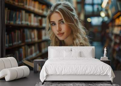 Attractive young blonde woman standing in a library aisle, focused on reading a book Wall mural