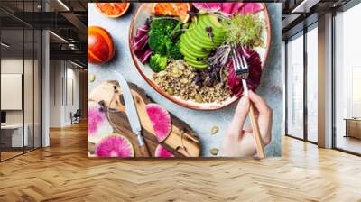 Girl holding fork and eating vegan, detox Buddha bowl with quinoa, micro greens, avocado, blood orange, broccoli, watermelon radish, alfalfa seed sprouts. Wall mural