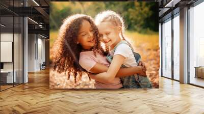 Two happy girls as friends hug each other in cheerful way. Little girlfriends in park. Wall mural