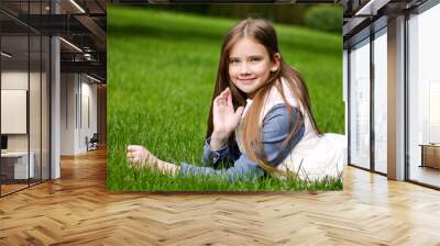 Portrait of adorable smiling little girl child preteen lying on grass in the park Wall mural