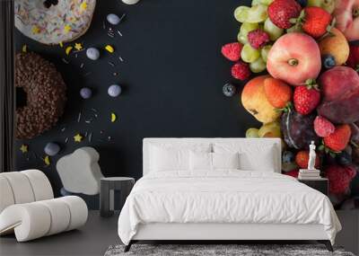 a lot of natural and healthy vitamin fruits, berries vs sweet and junk food on a black background. v Wall mural