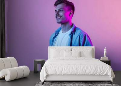 A young man in a jeans shirt and white t-shirt smiles as he gazes away against a vibrant purple gradient backdrop infused with neon light Wall mural